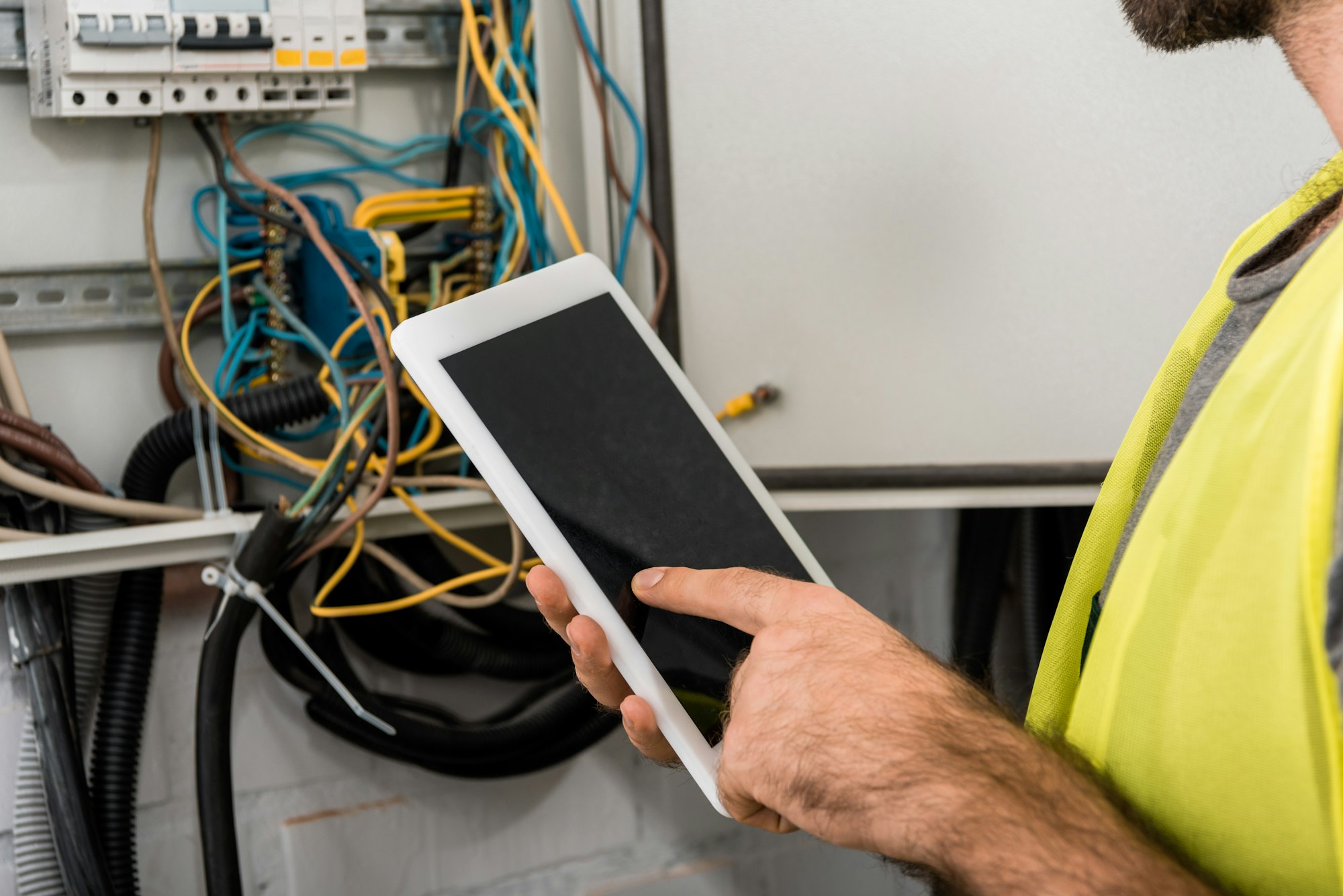 cropped image of electrician using tablet near electrical box in corridor