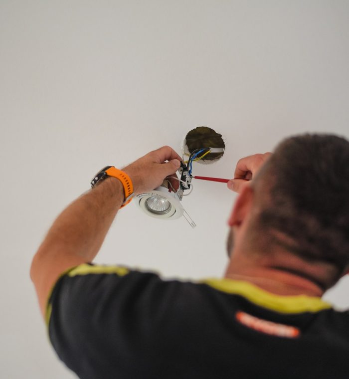 Back view of a handyman fixing electricity wires in a white wall