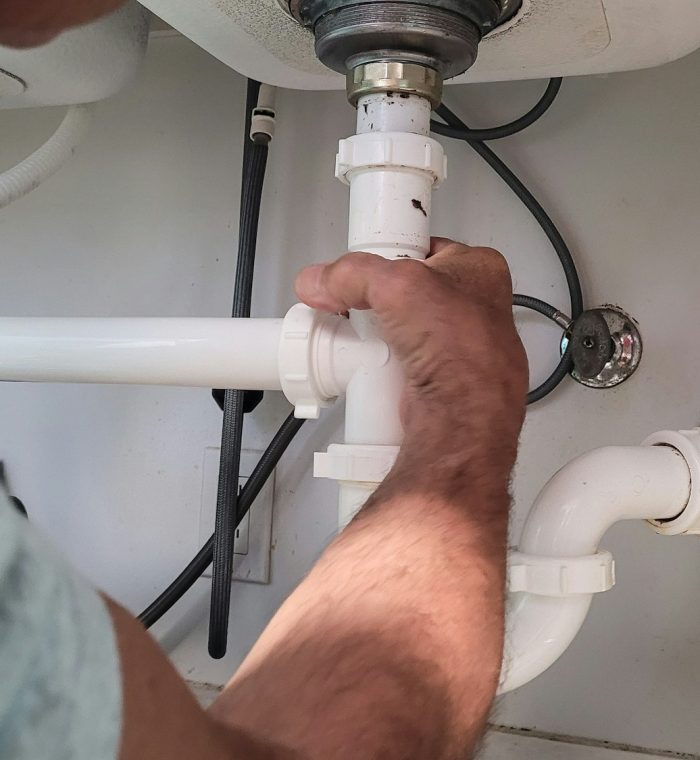 Handyman at home tightening seals on plumbing pipes to stop a leak at kitchen sink.
